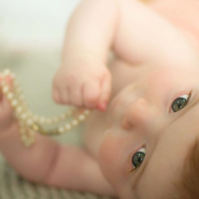 Close-up of a baby holding a string of pearls, capturing a tender and delicate moment.