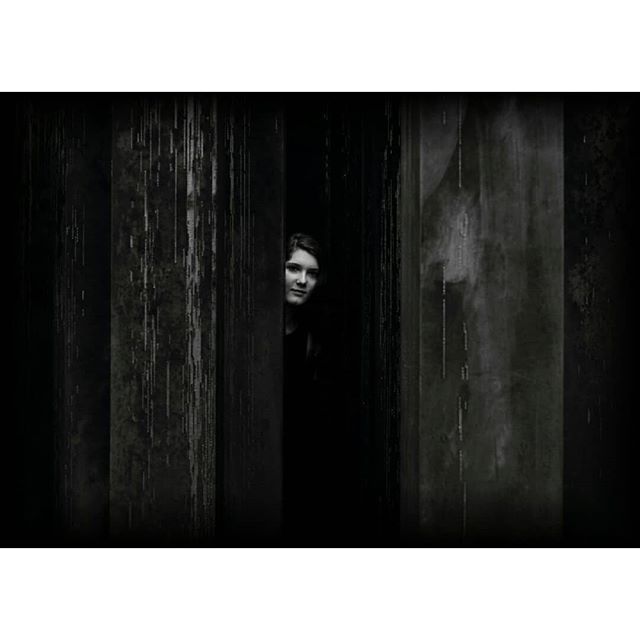 A woman emerges from the shadows in a moody, monochromatic portrait. 