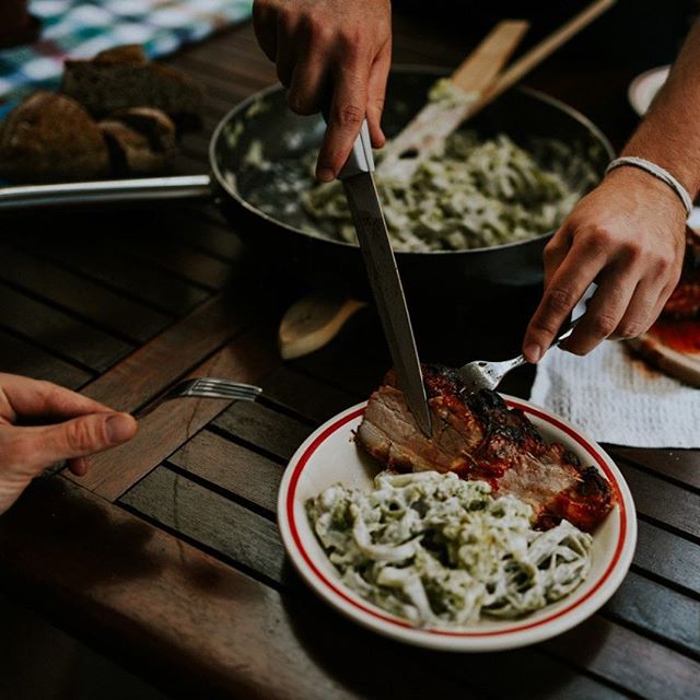 Close-up of a person cutting meat on a plate with pasta, showcasing an intimate dining setting.