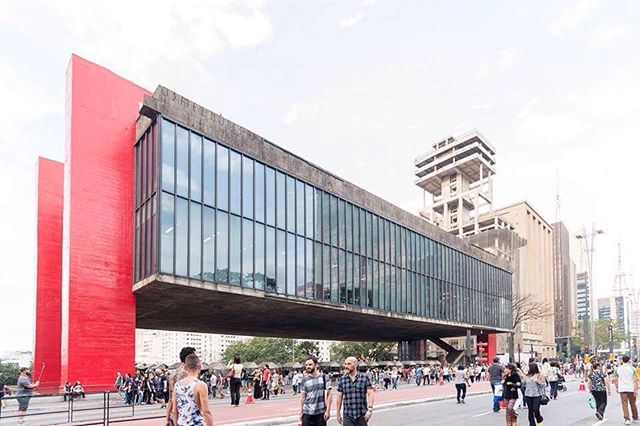 A modern building stands tall in a bustling city with many people walking on the street.