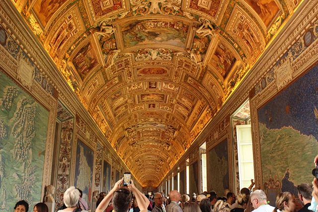 A grand hall with a highly decorated ceiling attracts many visitors in Vatican City. 