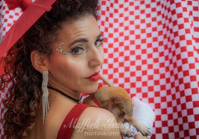 A woman poses with a small puppy, set against a red and white checkered backdrop.