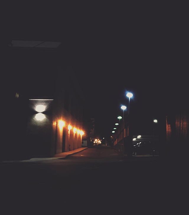 A dimly lit alleyway at night with streetlights and buildings, capturing a mysterious urban scene.
