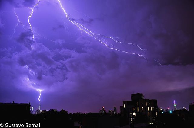 Lightning strikes light up the night sky over a city skyline during a powerful thunderstorm, creating a dramatic and intense scene.