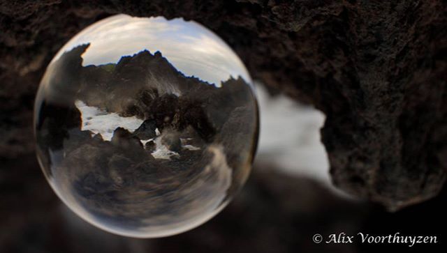 Coastal landscape reflected within a lensball, offering a tranquil and artistic perspective of the ocean and rocky shore.