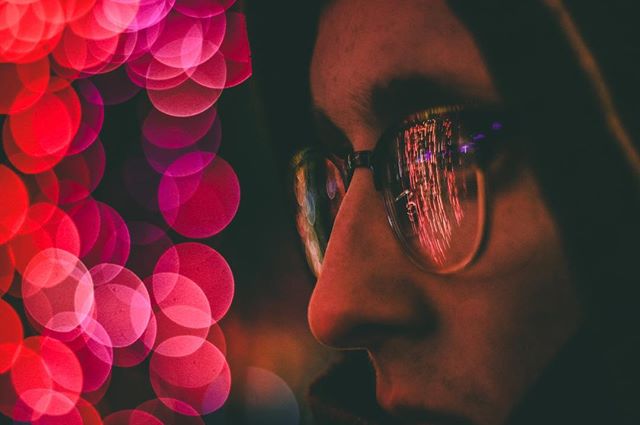 Close-up of a person wearing glasses reflecting city lights, showcasing an urban nightlife vibe.