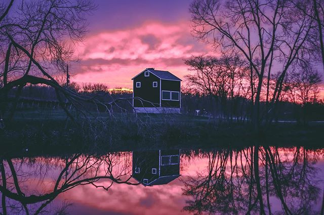 A tranquil image of a house reflecting in a lake at sunset with pink and purple hues creating a serene atmosphere.