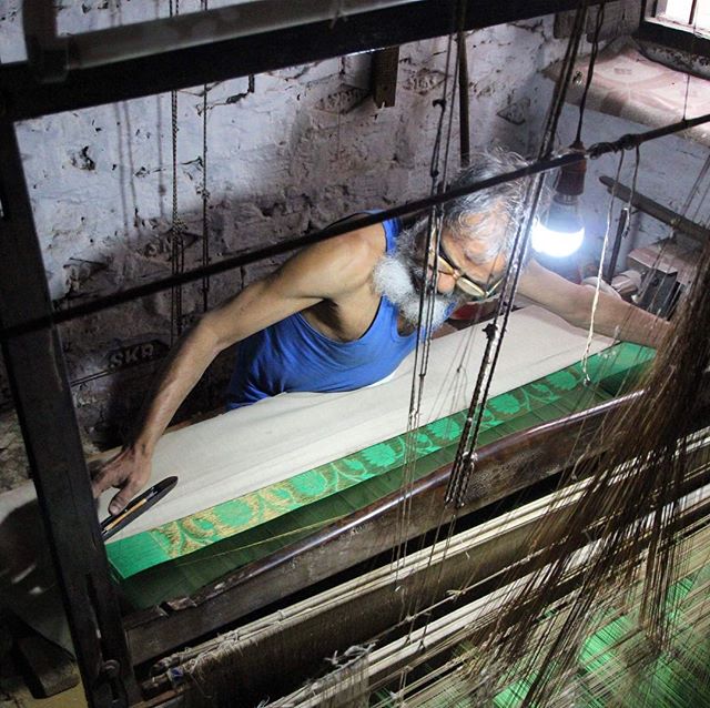 A weaver meticulously works on a traditional loom, crafting fabric in a small workshop, showcasing artisan craftsmanship.