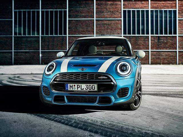 A blue Mini Cooper John Cooper Works with white stripes parked in an urban setting.