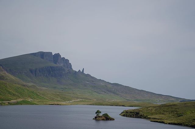 Scenic landscape of a loch with a small island and a mountain backdrop in the Isle of Skye, Scotland.