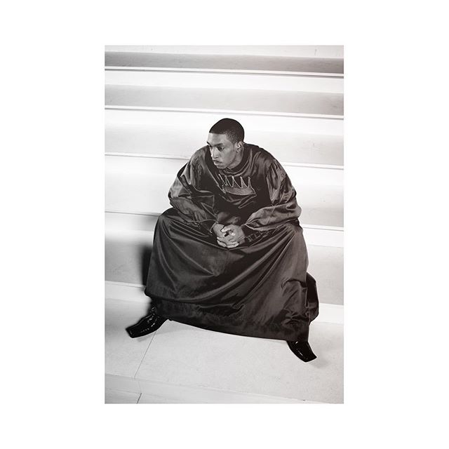 A man in a gown sits on the stairs in a monochrome shot, creating a contemplative scene.
