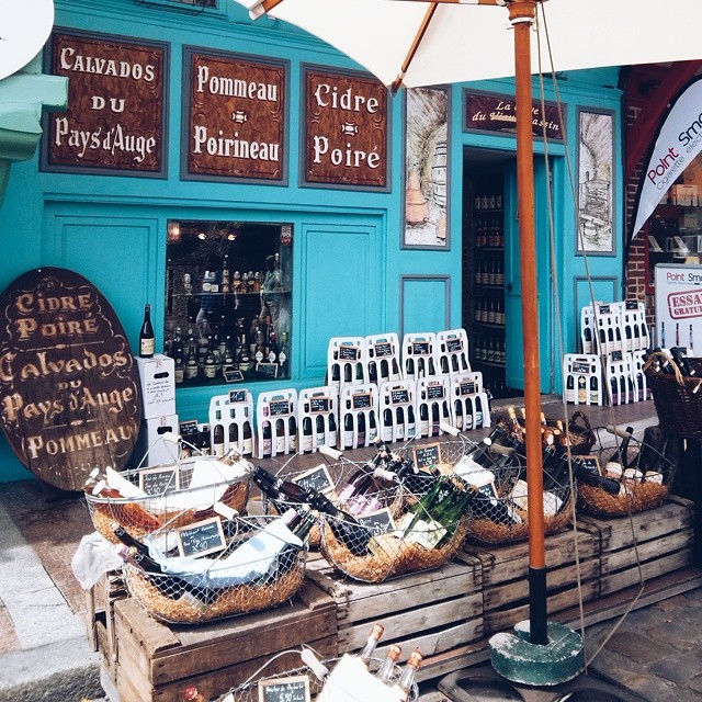A charming wine shop displays its products in rustic baskets outside a turquoise-painted store in a quaint town.