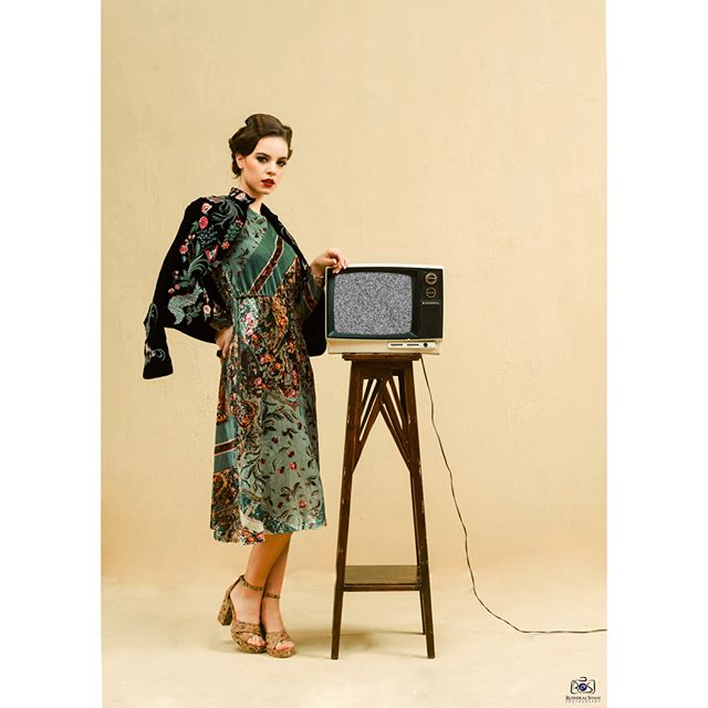A vintage-styled woman poses with an old television in an editorial fashion shot.