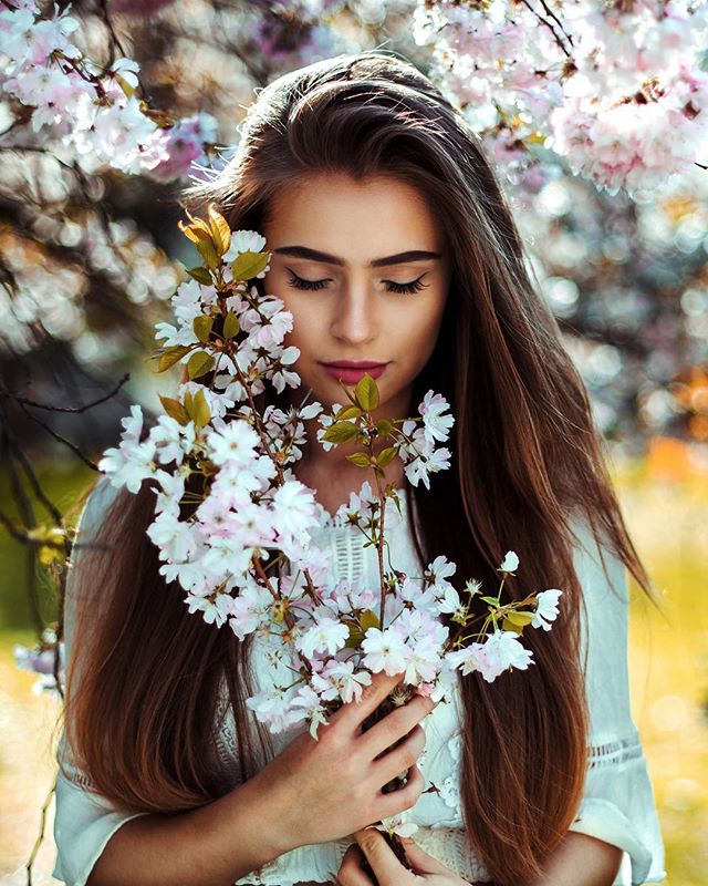 A woman gently holds spring blossoms, eyes closed, radiating serenity and natural beauty.