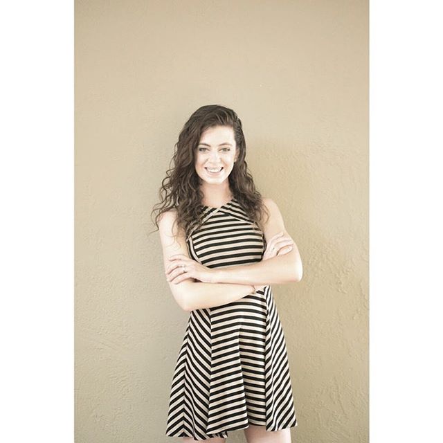 A smiling woman in a striped dress poses confidently in front of a neutral wall.