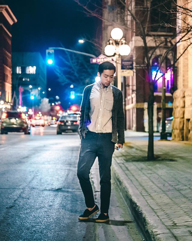 A stylish Asian man walks on a city street at night, showcasing urban fashion in a cool-toned environment.