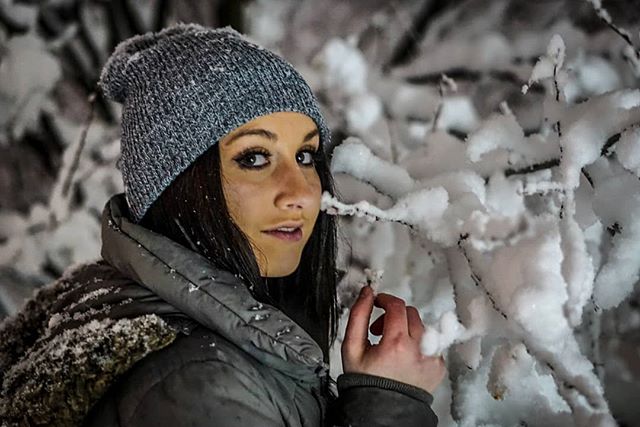 A woman in a beanie poses amidst snow-covered trees during winter.