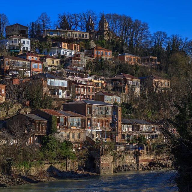 Scenic view of traditional houses nestled on a hillside by a river, exuding calm and timeless charm.
