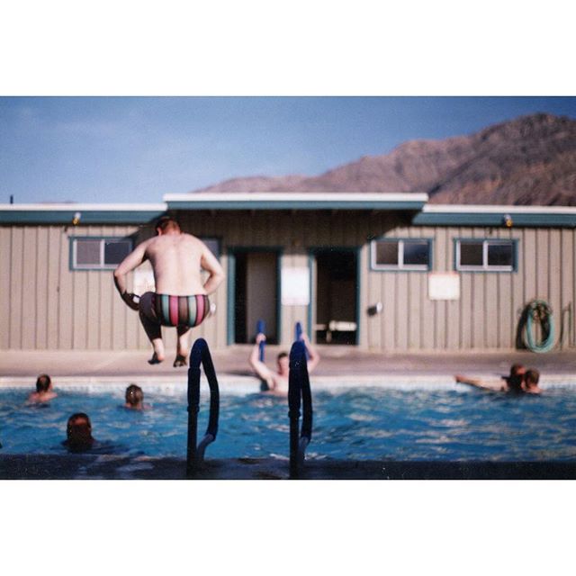 A group of people are enjoying a sunny day at the swimming pool, with one man jumping in.