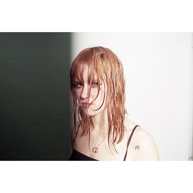 A woman with wet hair stares intensely at the camera in a moody portrait. 