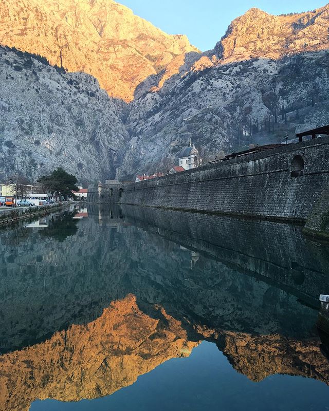 Scenic view of Kotor's fortress walls reflecting in the water, surrounded by mountains. A perfect travel destination.