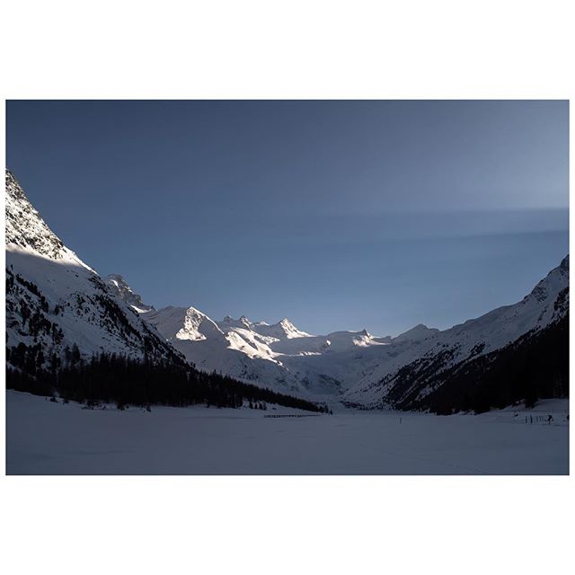A scenic winter landscape showcases snow-covered mountains and a peaceful valley under a clear sky.