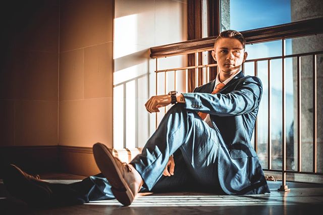 A man in a suit sits indoors by a window, bathed in natural light.