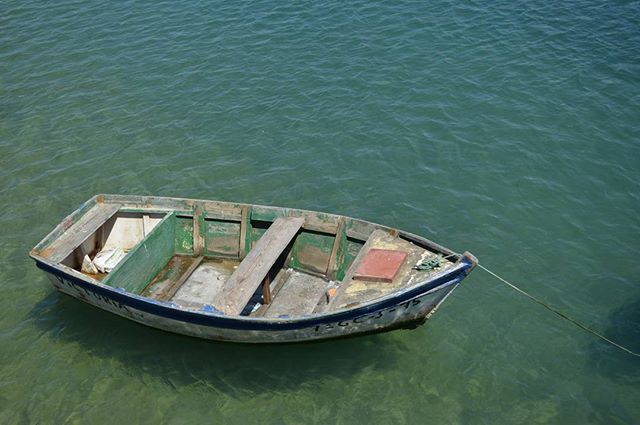 A small, weathered rowboat rests peacefully on calm, clear water under natural light, perfect for maritime or outdoor themes.