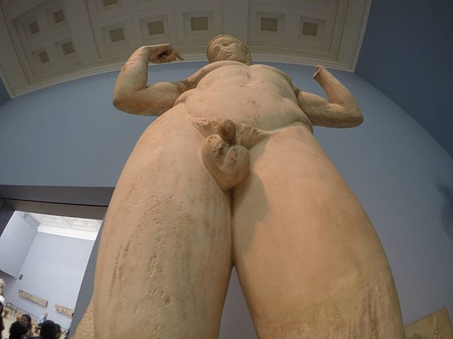 A low-angle shot captures a nude male sculpture in a museum, showcasing classical art and historical value.