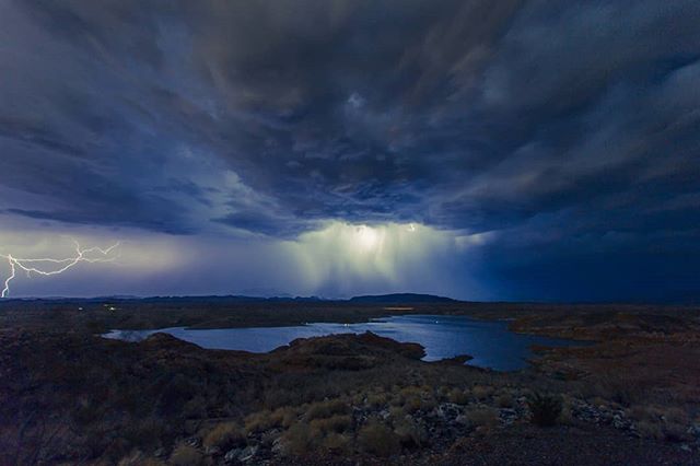 A dramatic landscape featuring a lake under a stormy sky with lightning strikes and heavy rain.