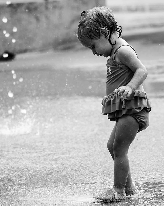 A young girl plays in a fountain, enjoying a moment of fun in black and white.