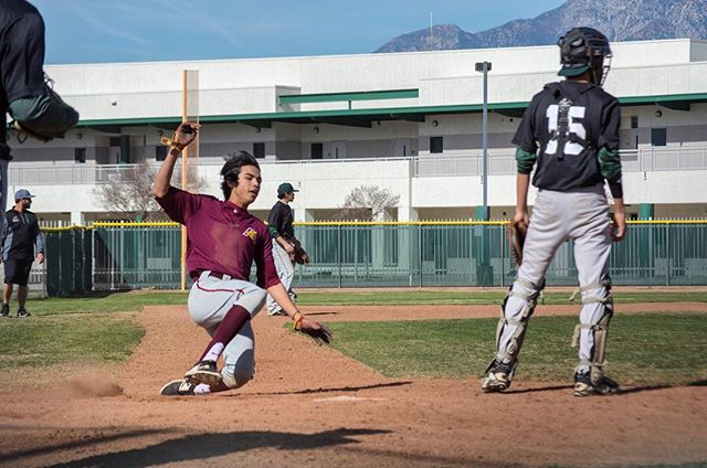A baseball player slides into base as the catcher prepares to catch the ball during a baseball game on a sunny day.