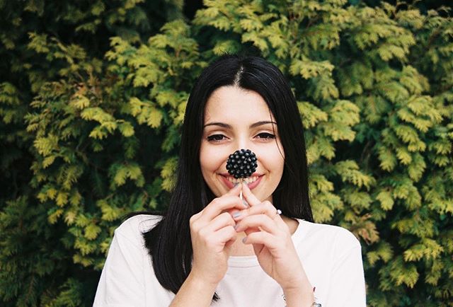 A cheerful woman playfully poses with a blackberry in front of a lush green backdrop.