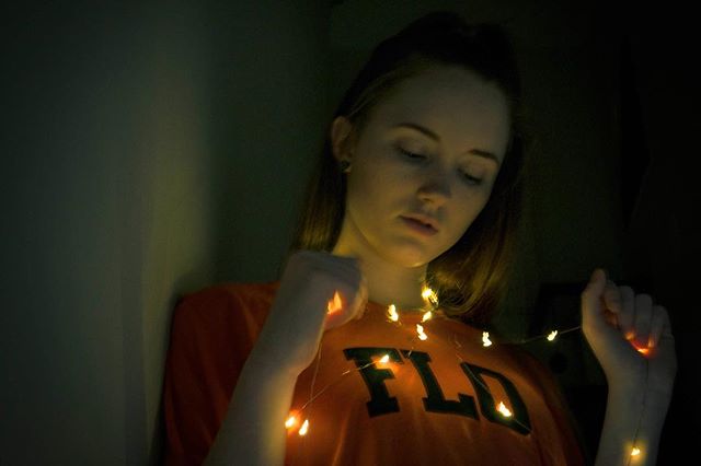 A serene woman gently holds fairy lights, creating a dreamy, intimate ambiance in a softly lit room.