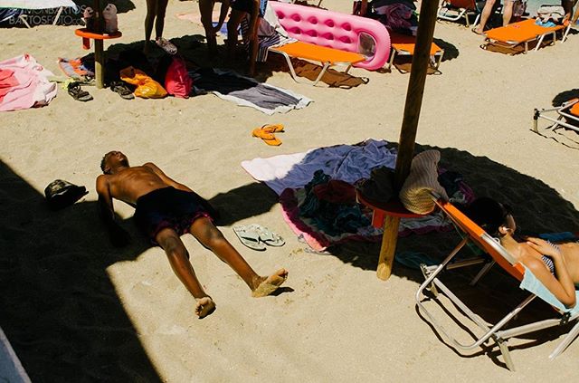 People relax on a sunny beach with lounge chairs and towels scattered across the sand.