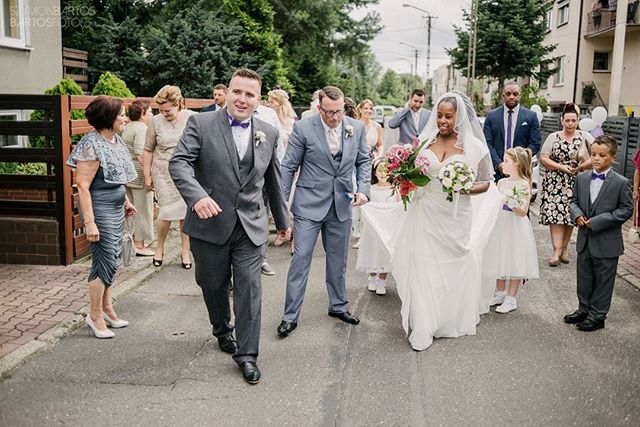 A wedding party walks down the street, celebrating the bride and groom with guests.