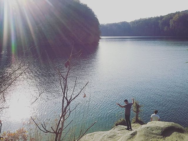 Two people enjoy the scenic view of a serene lake surrounded by lush greenery on a sunny day.