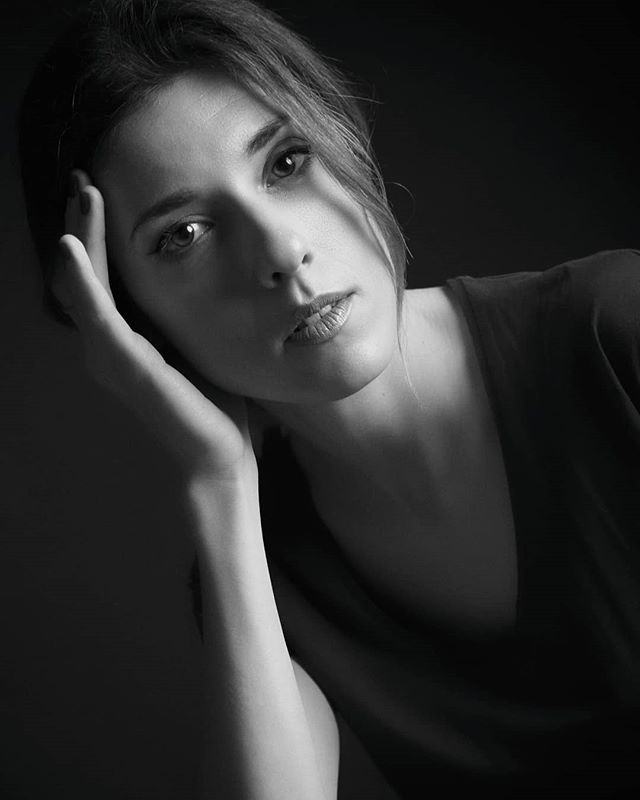 A woman poses in a close-up, black and white portrait with soft, natural lighting.