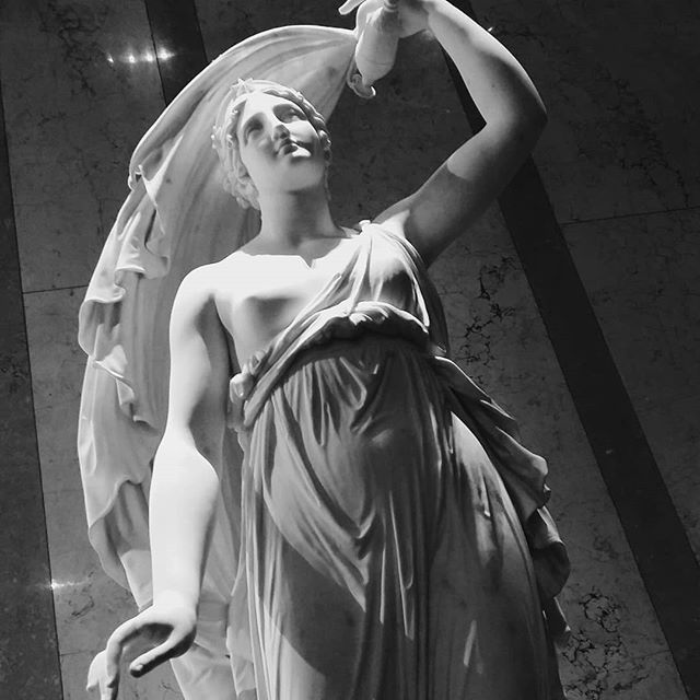 A monochrome statue of a woman in flowing robes is captured from a low angle.