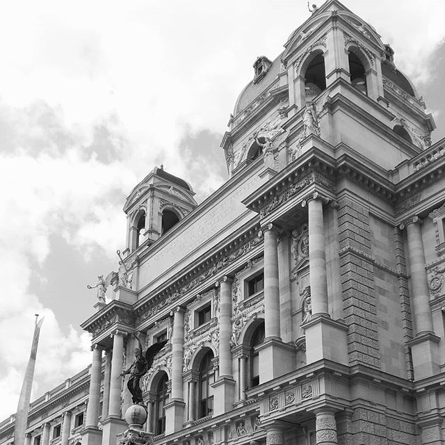 A black and white view of a classical building featuring statues and ornate architecture in an urban setting.