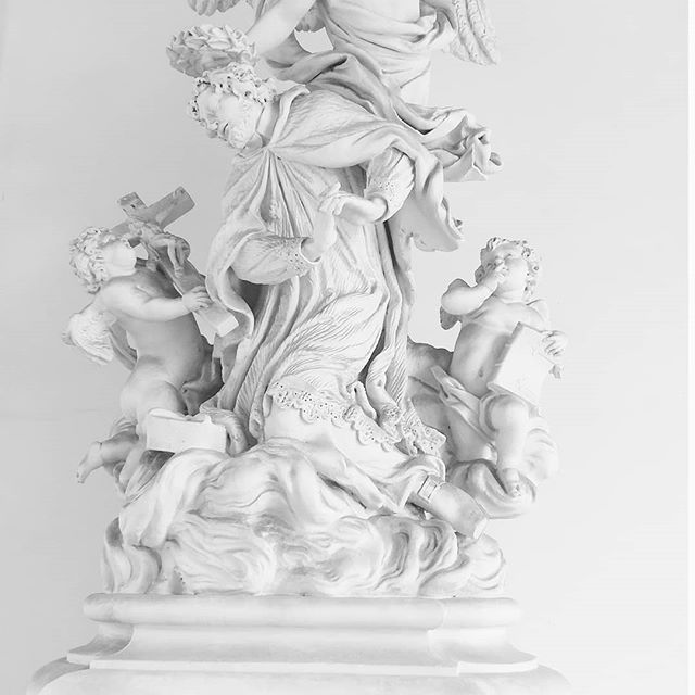 A monochrome sculpture featuring religious figures and cherubs, evoking a sense of serenity and classic artistry.