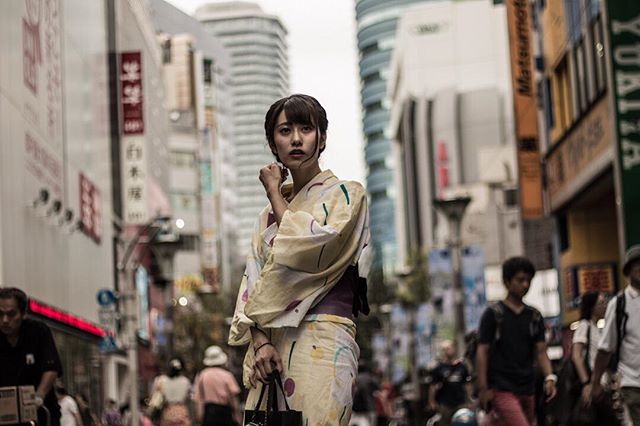 A woman in a yukata stands on a busy city street with buildings in the background.