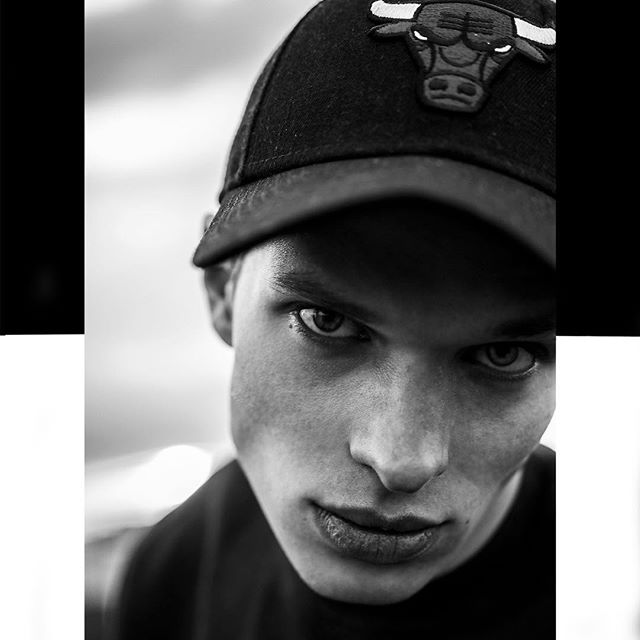 A monochrome portrait of a man in a Bulls cap, shot at a low angle with hard lighting for a confident, intense mood.