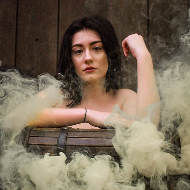 A dreamy portrait of a brunette woman surrounded by smoke against a wooden background.