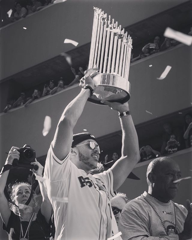 A baseball player triumphantly hoists the World Series trophy at a celebratory parade in black and white.