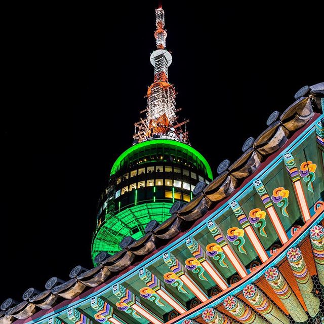 Namsan Tower in Seoul shines at night, framed by traditional Korean architecture.