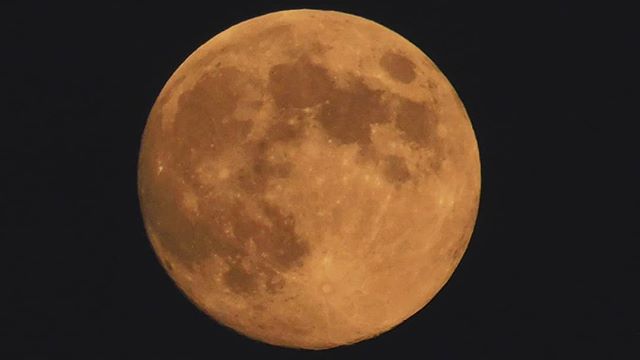 A full moon glows against a black sky, its surface detailed with craters and warm light.