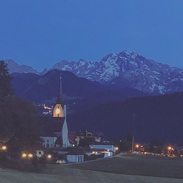 A picturesque village scene at night with a church and mountains in the background, creating a tranquil atmosphere.