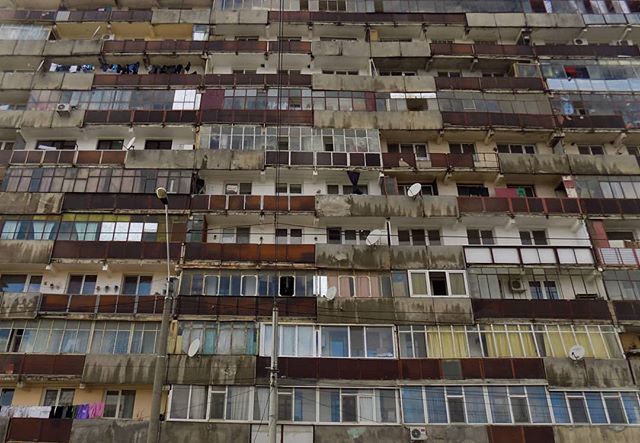 A multi-story apartment building facade with rows of balconies and windows creates a dense urban residential scene.