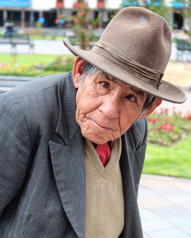 A senior man in a hat poses in a park setting, creating a cultural portrait.